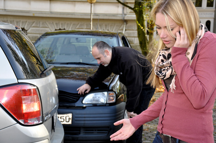 Eine junge Frau telefoniert nach einem leichten Unfall. Im Hintergrund ein Mann bei den Unfallwagen.